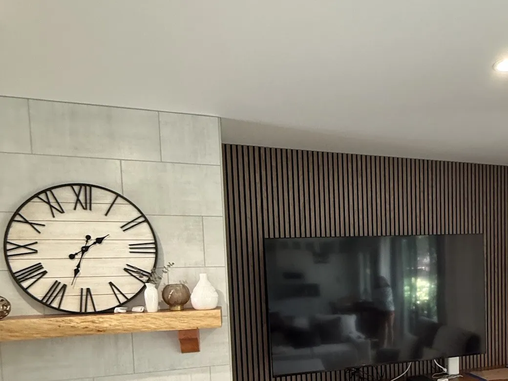 A living room feature wall in dark slatted timber beside a tiled chimney breast with a floating timber mantel