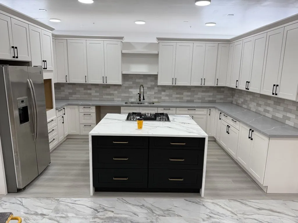 A finished kitchen with white shaker cabinets, a black island and stone counters